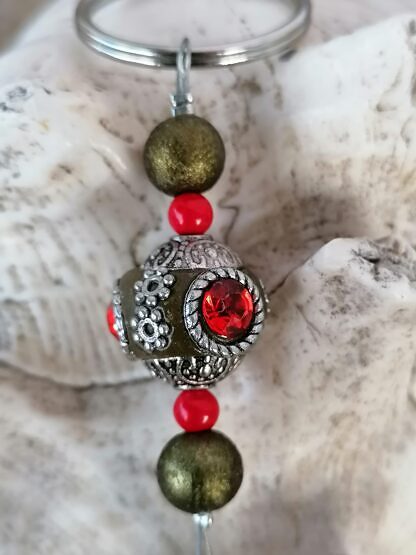 Yoga Schlüsselanhänger mit Kashmiri Perle lindgrün mit roten Strasssteinen olivgrünen Sternenstaubperlen roten Acrylperlen und Yoga Symbol Ajna Stirn Chakra